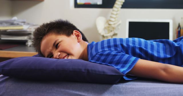 A young Asian boy appears uncomfortable or in pain while lying on a pillow, with copy space. His expression suggests he might be feeling unwell or experiencing discomfort.
