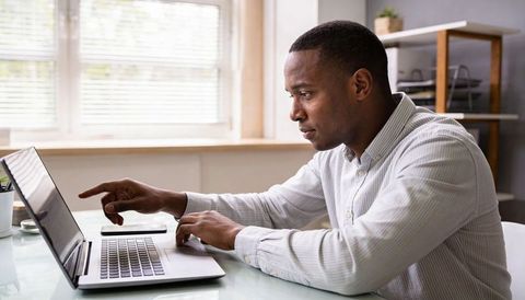 Focused professional pointing at laptop while working from home desk in bright daylight
