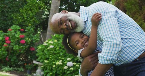 African American Grandfather and Granddaughter Embracing in Garden