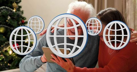 Senior couple sharing festive tablet video call with globe icons in cozy christmas room