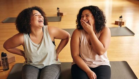 Laughing friends relaxing after yoga class on mats, promoting wellness and body positivity