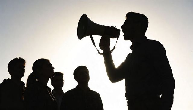 Silhouette leader speaking through megaphone to listening crowd at sunset