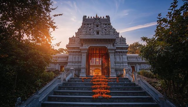 Sunset-lit stone temple gateway with marigold garlands draping carved steps and facade
