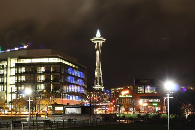Seattle's iconic Space Needle shines brightly against a night sky. Surrounding buildings are lit up, creating a vibrant, urban atmosphere. Perfect for use in travel brochures, tourism websites, and city-themed events.