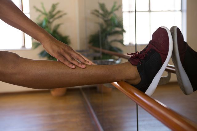 This image shows a male dancer stretching his leg on a barre in a studio. It is ideal for use in content related to dance, fitness, exercise routines, flexibility training, and healthy lifestyles. The indoor setting and the focus on the dancer's leg and shoe make it suitable for promoting dance studios, workout programs, and athletic wear.