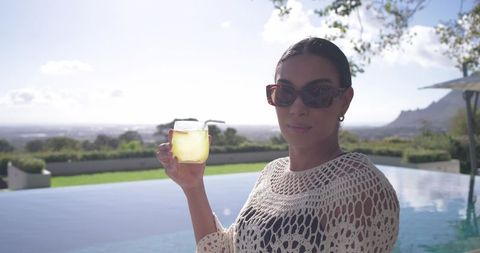African american woman relaxing at infinity pool holding drink in crochet cover-up sunglasses