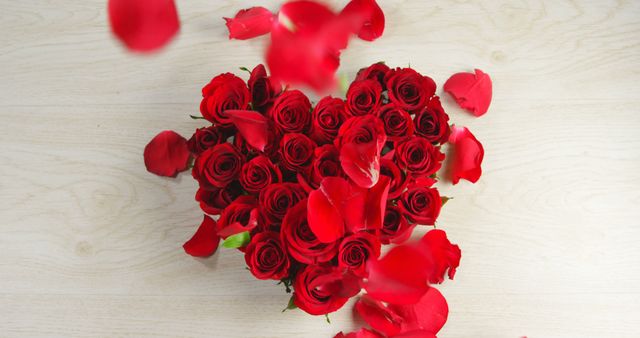 Red roses arranged in a heart shape with petals falling on a light wooden surface. Ideal for use in romantic and love-themed designs, including Valentine's Day cards, wedding invitations, anniversary announcements, and decorations that express affection and beauty.
