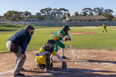 Youth baseball batter bunting while pitch crosses plate, catcher and umpire on sunny field
