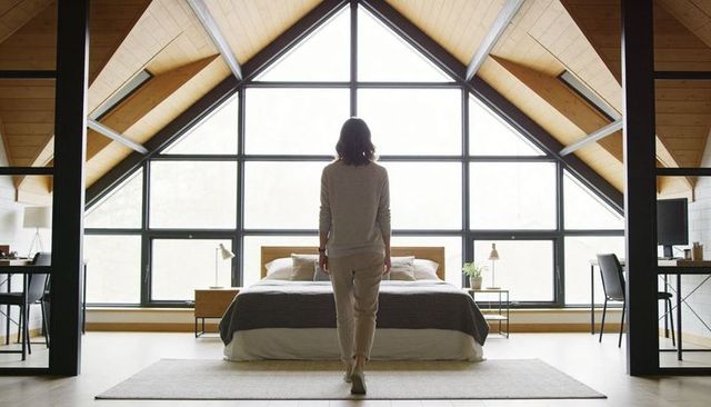 Woman standing facing triangular window in minimal a-frame loft bedroom