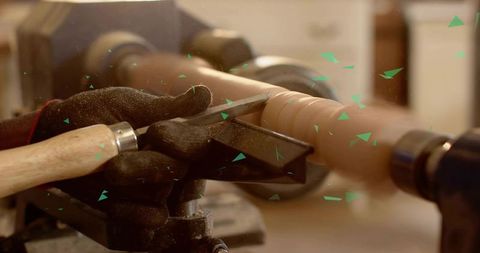 Woodworker shaping turned spindle on lathe with chisel and gloved hands, workshop craft