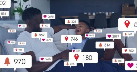Father and son laughing on sofa with laptop surrounded by social media notification icons