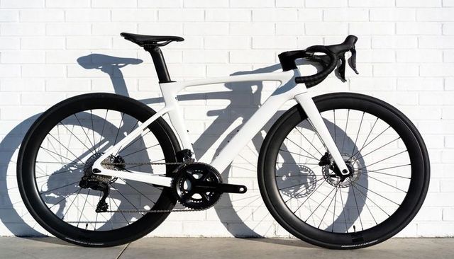 White aerodynamic carbon road bike with deep black rims and minimalist urban shadow