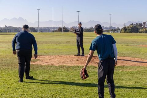 Pitcher preparing glove while teammates walking in on sunny baseball practice field