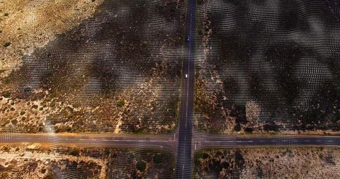 Four-way paved crossroads crossing arid scrubland with dotted grid pattern and car