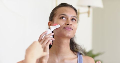 African american woman using handheld led facial device at vanity for skincare routine