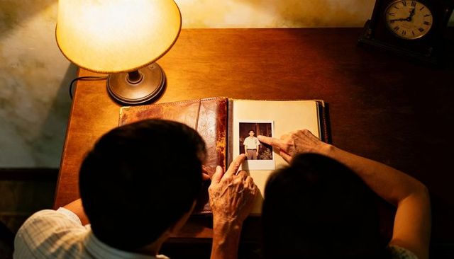 Senior couple reminiscing over vintage polaroid album under warm lamp light