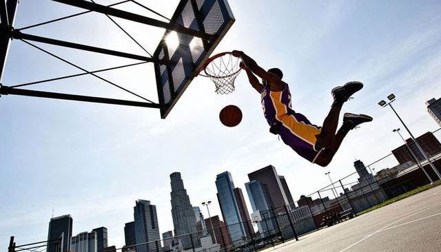 Explosive dunking athlete soaring over urban skyline on outdoor basketball court