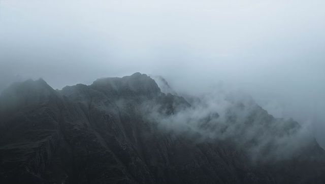 Misty jagged mountain ridge cutting through alpine clouds and swirling mist