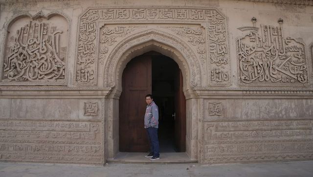 Traveler standing at carved islamic archway with arabic calligraphy and stonework