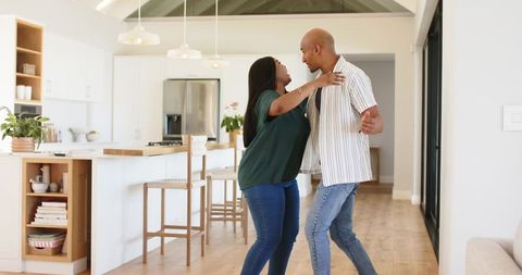 African American couple dancing and embracing in modern open-plan kitchen on wooden floor