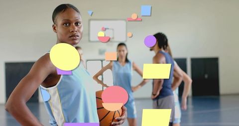 Confident female basketball player holding ball, standing on indoor court with teammates