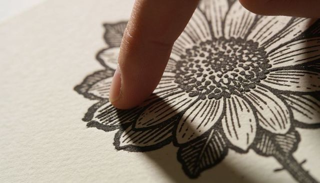 Closeup tracing fingertip along black ink floral illustration on textured cream paper