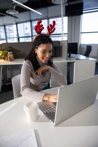 African american woman working on laptop wearing festive reindeer antlers in modern office