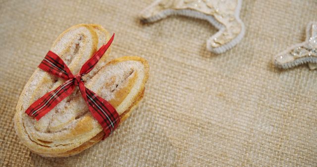 A delicious-looking pastry tied with a festive red ribbon lies on a textured surface, with copy space. The ribbon adds a touch of holiday cheer, suggesting this treat could be a sweet gift or a festive dessert option.