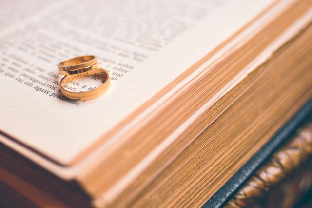 Two gold wedding bands rest on the open pages of a book. The intimate arrangement symbolizes romance, commitment, and the timeless nature of love, making it suitable for use in wedding invitations, literary art, and articles related to love and relationships.