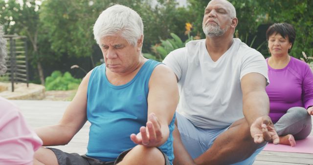 Seniors sitting in lotus positions practicing outdoor yoga meditation. They are focusing on their breathing and mindfulness. This image is ideal for use in promoting fitness and wellness programs for seniors, yoga and meditation classes, health and wellbeing articles, and advertisements for senior living or community centers.