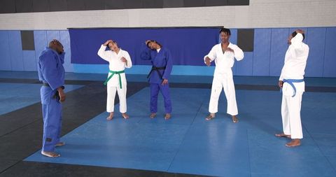 Diverse judo group stretching necks in dojo wearing traditional gis