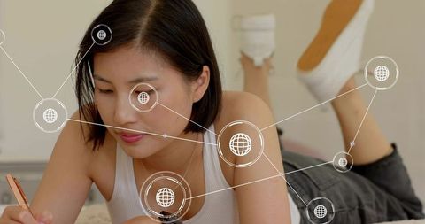 Young Asian woman writing on bed with global network overlay, studying and planning future