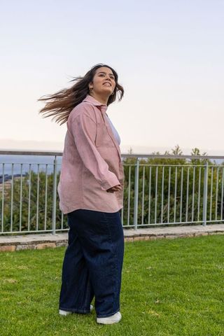 Young woman enjoying ocean breeze wearing pink shacket and wide-leg denim at overlook