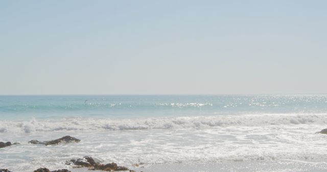 View of an empty beach with waves crashing on the rocks and cloudless blue sky - Download Free Stock Photos Pikwizard.com