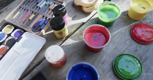 Assorted art supplies including paint pots, brushes, and color palette on a wooden table. Perfect for illustrating themes of creativity, artistic endeavors, and school projects. Ideal for educational materials, art and craft promotion, and creative workshops.