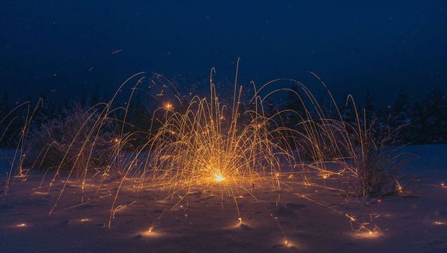 Erupting spark fountain sending golden arcs across snow-covered field during blue hour