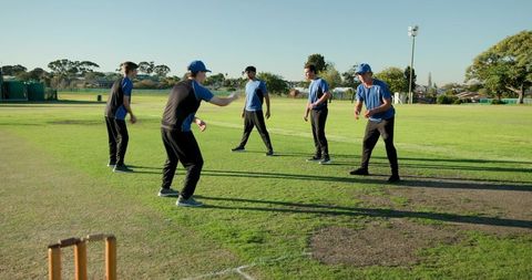 Youth cricket team practicing fielding drill on suburban outfield with wooden stumps