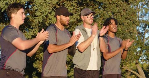 Multiracial male teammates clapping on sidelines celebrating player arrival, teamwork