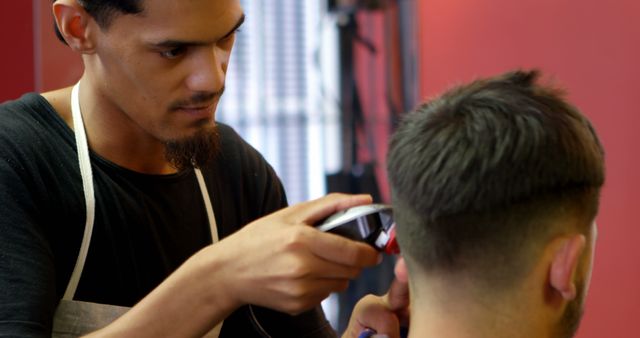 Young biracial man giving a haircut in a barbershop setting. Precision is key as the barber shapes his client's hairstyle with care.