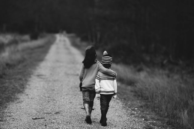 Two children, likely siblings, are walking on a country path embracing each other, emphasizing themes of togetherness and companionship. The absence of color directs focus on their bond and the serene rural environment. Ideal for use in themes of childhood, family bonds, friendship, or nostalgia.