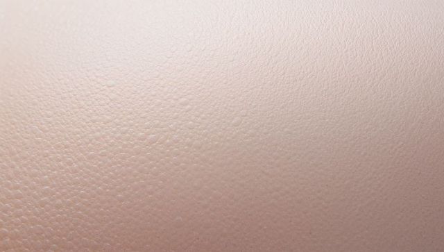 Macro closeup of pale pink pebbled skin-like texture showing fine pores and tiny droplets