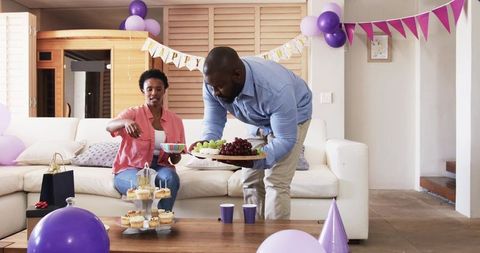 African American couple preparing cozy birthday celebration with balloons and cupcakes
