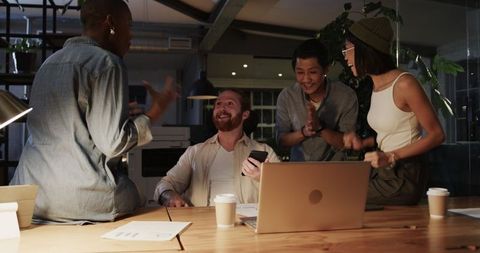 Dynamic Team Celebrating Digital Success Around Office Laptop