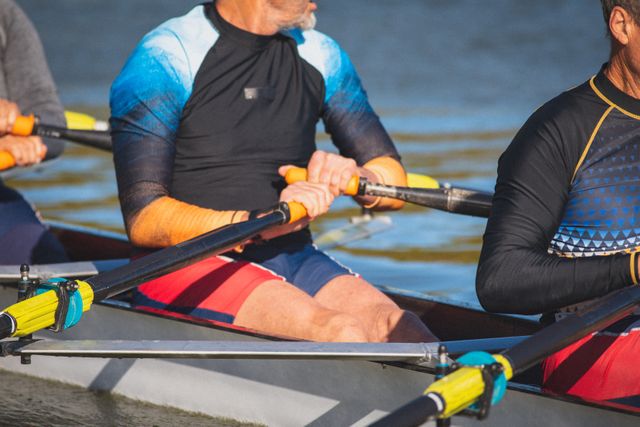 Midsection of senior caucasian man and rowing club team sitting in boat on river holding oars. senior sports hobby, active retirement lifestyle.