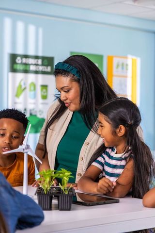 Diverse female teacher guiding kids building wind turbine and planting seedlings