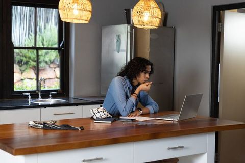 Non-binary adult studying at kitchen island with laptop and paperwork