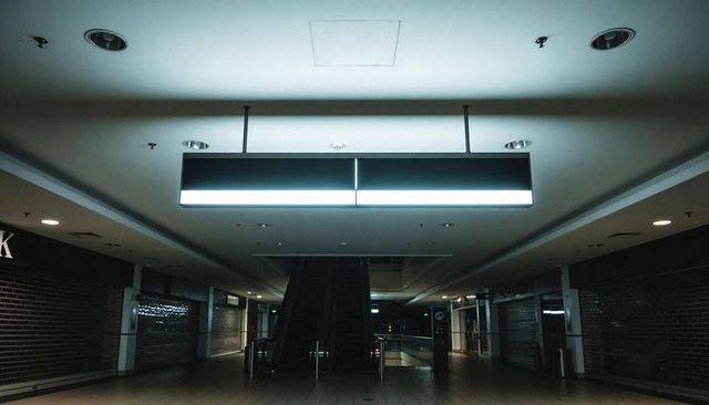 Empty mall corridor glowing with cool blue ceiling light above closed escalator at night