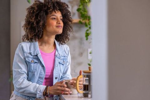 African american woman in denim jacket holding mug by french press in sunlit cafe morning
