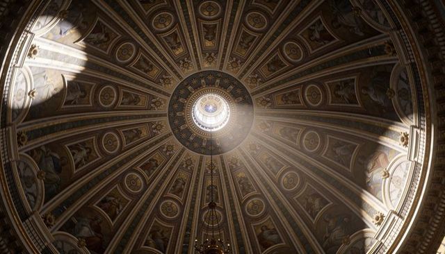 Sunlight streaming through oculus onto ornate cathedral dome featuring gilded frescoes and chandelie