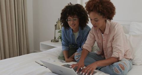 Friends collaborating on laptop while sitting on bed, planning project and studying